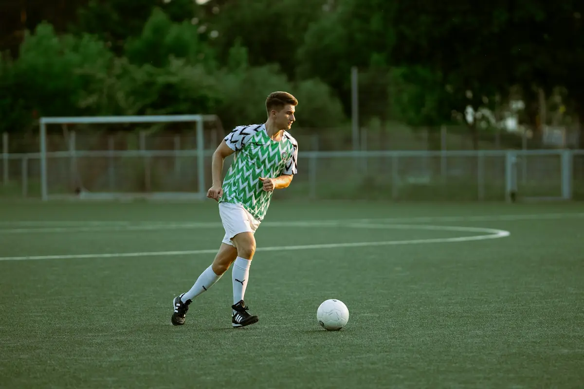 Jugador de fútbol conduce el balón en un campo de césped.