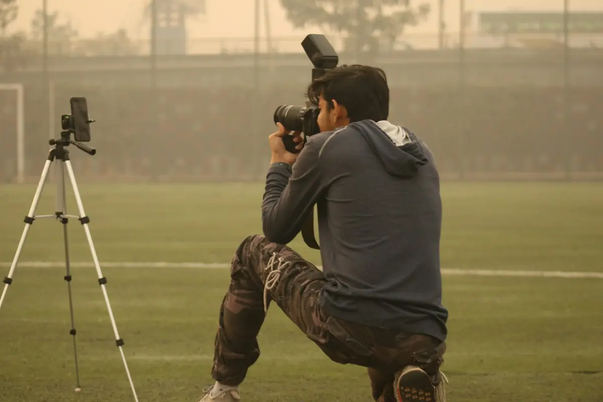 Un fotógrafo deportivo con cámara y trípode junto al campo.